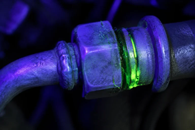 Technician inspecting a car AC refrigerant circuit with ultraviolet leak-detection dye