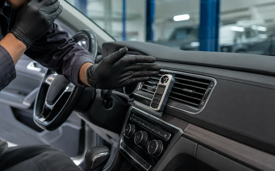 Technician checking dashboard vents while diagnosing a car AC hissing noise