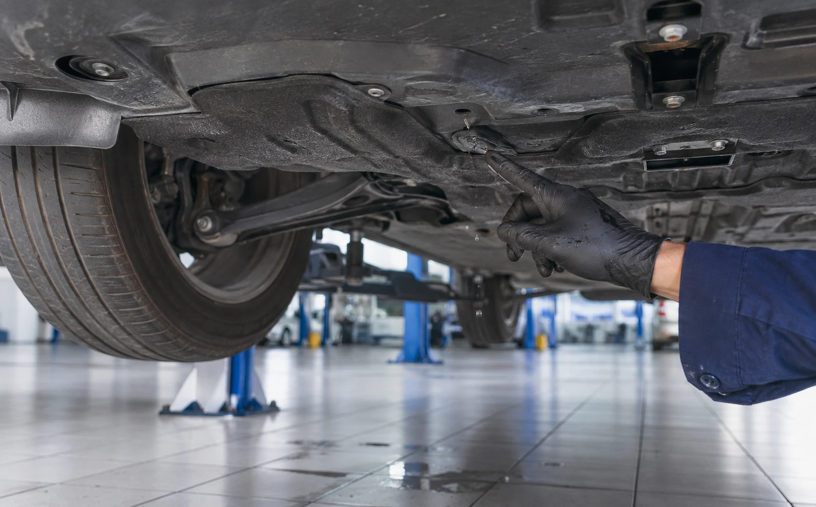 Technician inspecting the car AC evaporator drain outlet beneath a raised vehicle